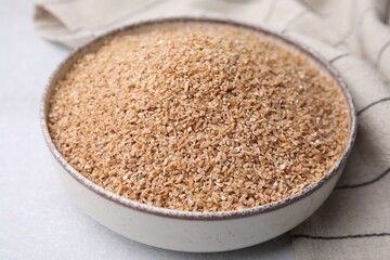 Dry wheat groats in bowl on light table, closeup