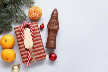 Composition with chocolate Santa Claus candy, Christmas gift, decor and tangerines on grey background
