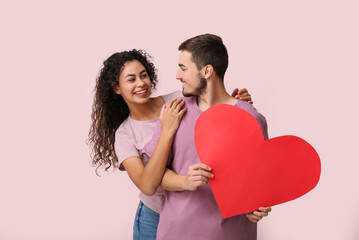 Young couple with red heart for Valentine's day on pink background
