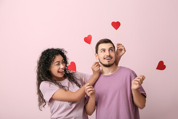 Funny young couple with paper hearts for Valentine's day on pink background