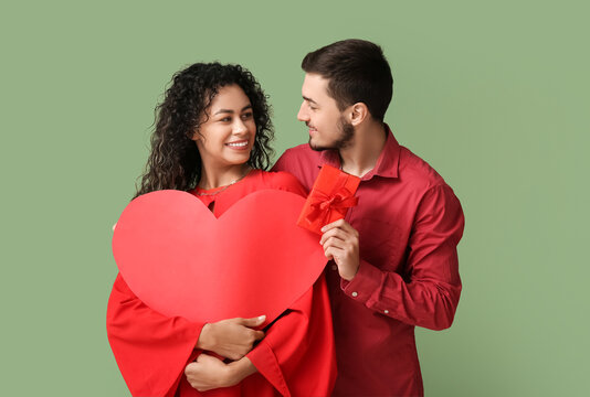 Young couple with red heart and gift for Valentine's day on green background