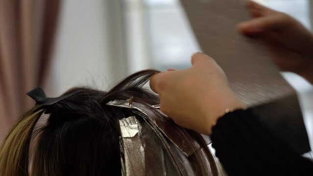Professional hairdresser dyes hair blonde highlights close-up in beauty salon