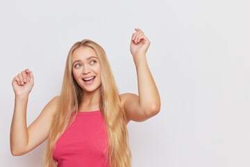 Happy young woman with long fair hair dancing with hands up on studio background, young people concept, copy space