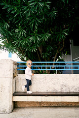 Little girl stands on a bench near the garden fence