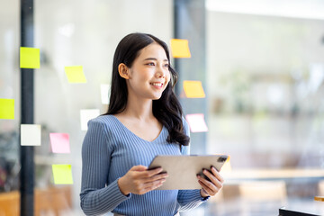 Happy asian businesswoman planning new project with sticky note in a creative writing on blank office glass