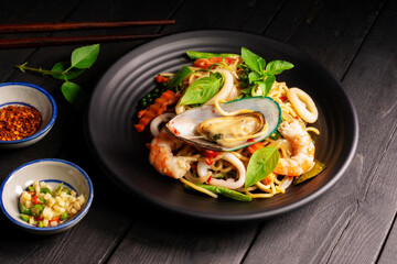 Seafood drunken spaghetti with shrimp squid clams chili, and basil. Thai food. Healthy Asian in a plate on a black background table. Top view.