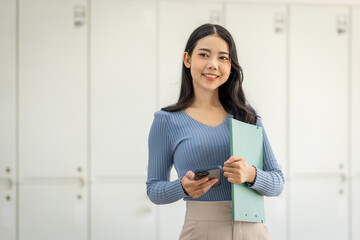 Asian business woman inside the office using the phone, the boss is holding a smartphone with a document in her hand