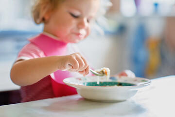Adorable baby girl eating from spoon vegetable noodle soup. Healthy food, child, feeding and...