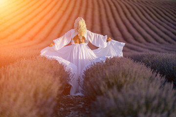 Blonde woman poses in lavender field at sunset. Happy woman in white dress holds lavender bouquet. Aromatherapy concept, lavender oil, photo session in lavender