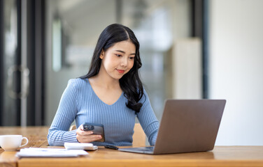 Portrait of Asian young female working on laptop with phone at the office