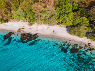Koh Samet Island Thailand, aerial drone view from above at a couple of men and woman on the beach of Samed Island in Thailand with a turqouse colored ocean and a white tropical beach