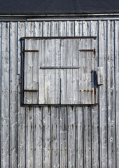 Weathered wooden siding with a closed window shutter, as a rustic background
