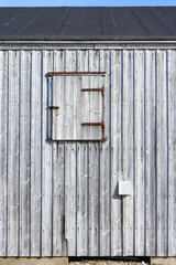 Weathered wooden siding with a closed window shutter, as a rustic background
