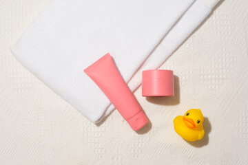 A tube of facial cleanser, a jar of lotion, a towel and a silicone duck are displayed on a white fabric background. Blank label for lettering design. Copy space for cosmetics advertising.