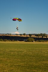 Isolated skydiver with bright colorful parachute landing to the field during sunny day, Klatovy,...