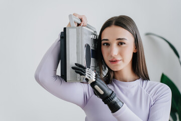Adorable girl with cyber hand holds old fashion audio layer looks at camera against wall. Female...