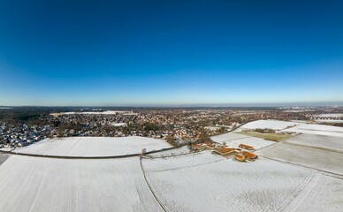 Wide panoramic view of a winter landscape with snow white fields and a village in the background