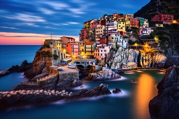  a picture of a town on a cliff by the ocean at night with lights on the buildings and the water in the foreground.