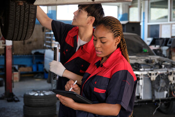 Young expert Black female inspects repair checklist with automotive mechanic worker partner, quality suspension technician team at fix garage. Vehicle maintenance service works industry occupation job
