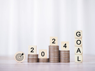 Wooden block with word GOAL and number 2024 on stack of coins. The concept of saving money for...