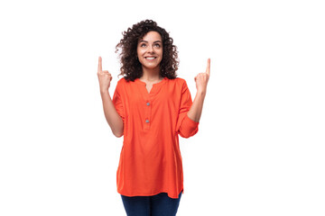 young curly brunette lady dressed in a stylish bright orange shirt gesticulates pointing her finger...