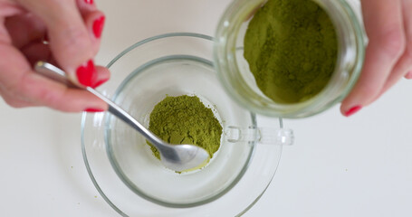 Woman is putting matcha powder in glass cup by the spoon