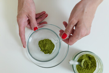 Woman's hand is holding glass cup with matcha powder, top view