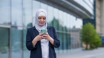 Business woman in hijab and suit using smartphone outdoors. 