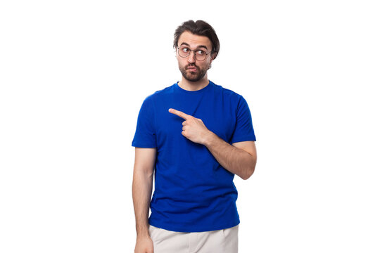 A 30 year old surprised European guy with black hair and a beard in a blue T-shirt points to the space for advertising
