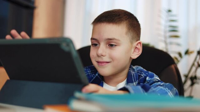 Caucasian male child dressed in casual clothes using digital tablet in black case for doing homework. Concentrated kid with focused expression responsibly behaving on e-learning using modern gadget.