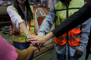 A group of people in a factory are holding hands, showing unity and teamwork in their industrial...