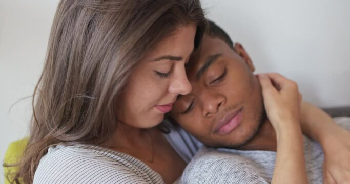 Close up of attractive young couple holding each other tenderly on couch. African American millennial man resting on Caucasian girlfriend. 4k slow motion handheld