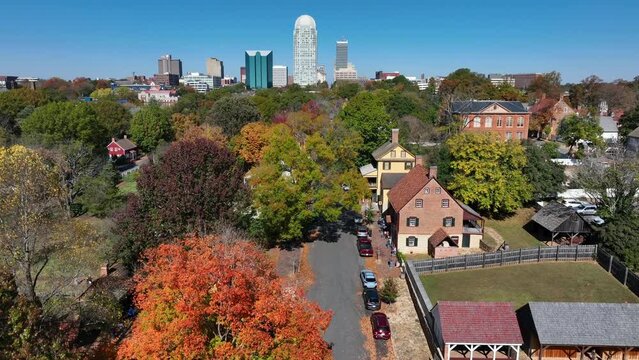 Old Salem in autumn. Aerial rising shot revealing modern skyline of Winston-Salem, North Carolina.