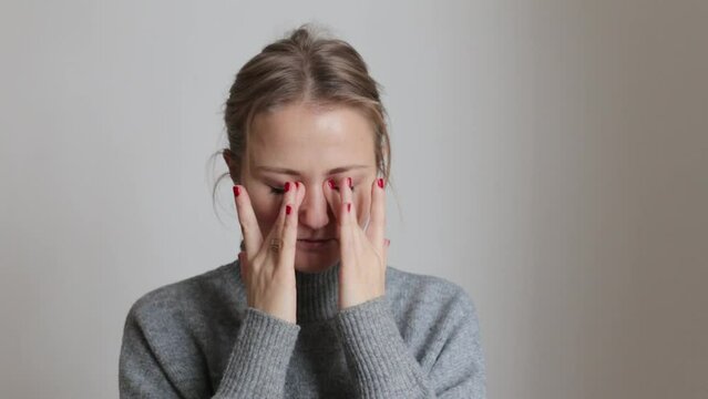 A young girl in a cozy gray sweater rubs her eyes from fatigue. The girl rubs her eyes.