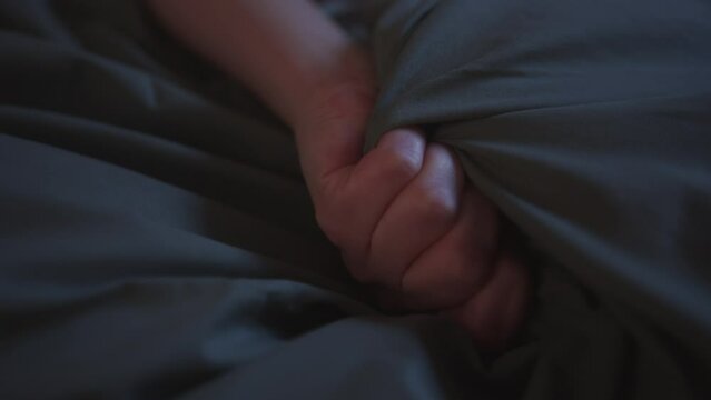 Woman clinging to the sheets enjoying a pleasurable orgasm. Hands close up
