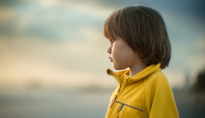 Closeup portrait of boy child daydreaming at the ocean. Shallow DOF, blurred background, copyspace.