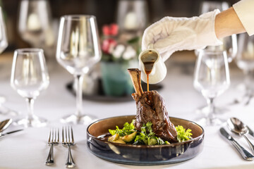 The chef or waiter finishes the meal right on the restaurant table, pouring the sauce over the leg of lamb confit - obrazy, fototapety, plakaty