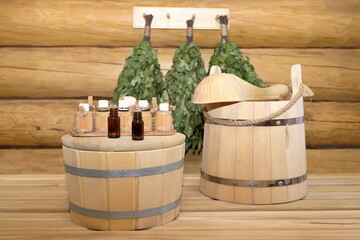Bottles of healing essential oil are on cover of a wooden vat standing next to wooden bucket with...