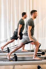 Fit men doing pilates exercises on reformer beds at gym
