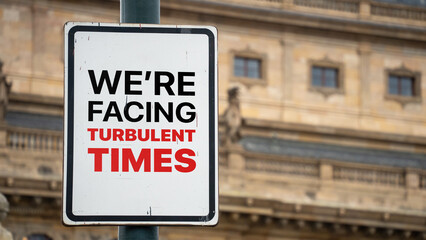 Obraz premium We're facing turbulent times on a sign in a city business district