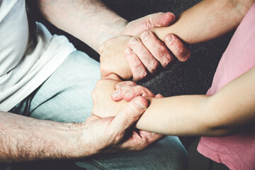 The hands of an elderly man hold the hands of a child. Close-up of grandfather and granddaughter...
