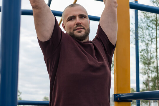 athlete on the horizontal bar. a pumped up bald man with a beard is doing pull-ups on a high iron horizontal bar on the playground, sports concept