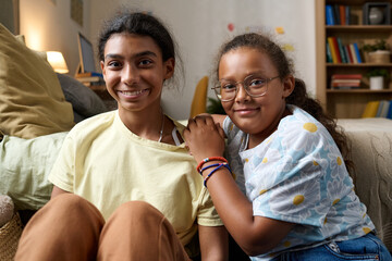 Portrait of two sisters smiling at camera while sitting on the floor in their room