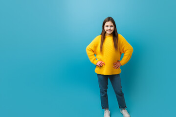 girl model. a little girl with long hair stands in a warm yellow sweater and jeans on a blue background