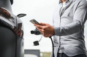 Man Holding Power Charging Cable For Electric Car In Outdoor Car Park