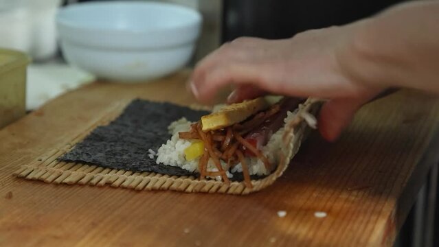 김발 위에 김 흰밥 햄 어묵 단무지 우엉 계란을 올려 돌돌 말아 만든 김밥을 칼로 썰어 접시에 담은 모습