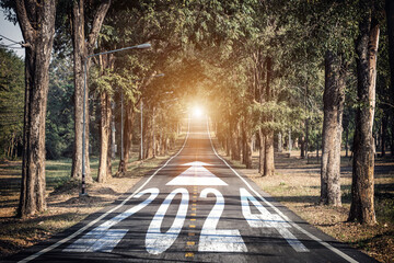 New year 2024 plans with vision concept. number 2024 written on the middle of asphalt road with arrow sign pointing forward and sunlight for start and reach new goals and achievements for year 2024.