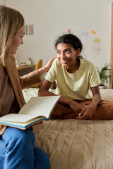 Vertical image of social worker talking to adoptive child and making notes in notebook while they...