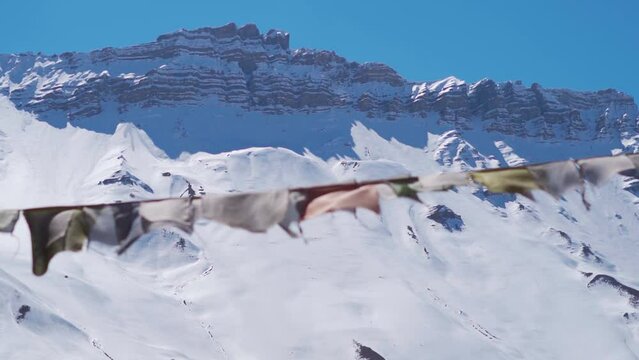 Slow motion rack focus shot of prayer flags in front of snow covered Himalayan mountain peaks at Spiti Valley in Himachal Pradesh, India. Focus changes from flags to the mountains in background.