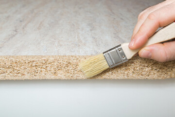 Man hand holding paint brush and applying waterproof glue on cut tabletop hole or edge. New surface...